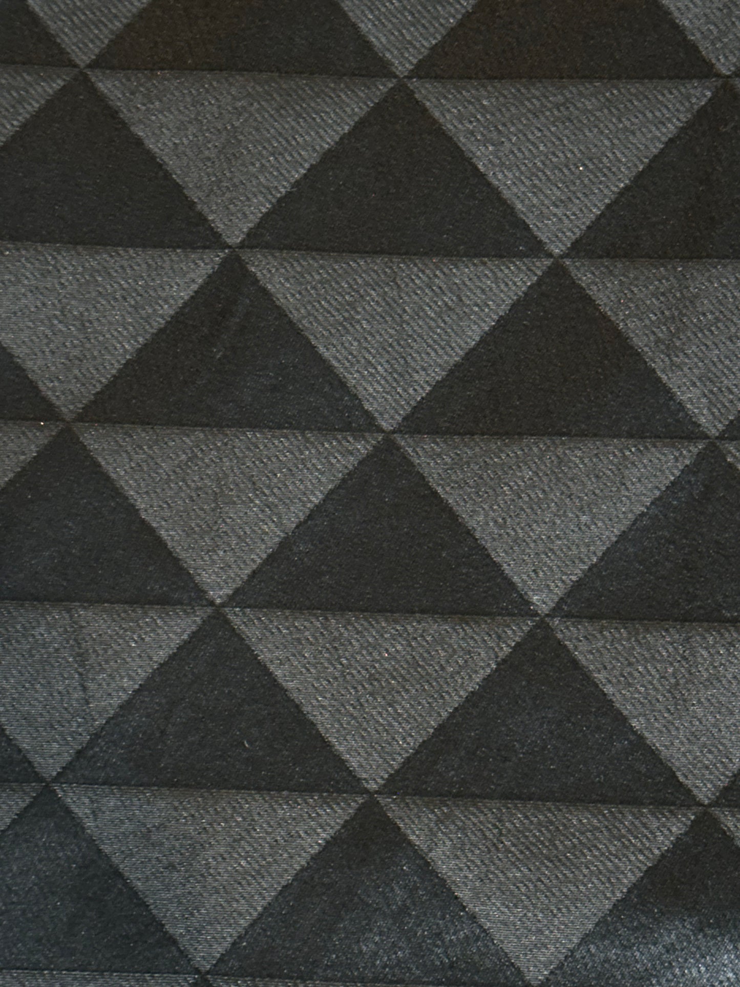 A close-up of a woven fabric with a repeating geometric pattern of interlocking triangles in dark charcoal gray and medium gray.