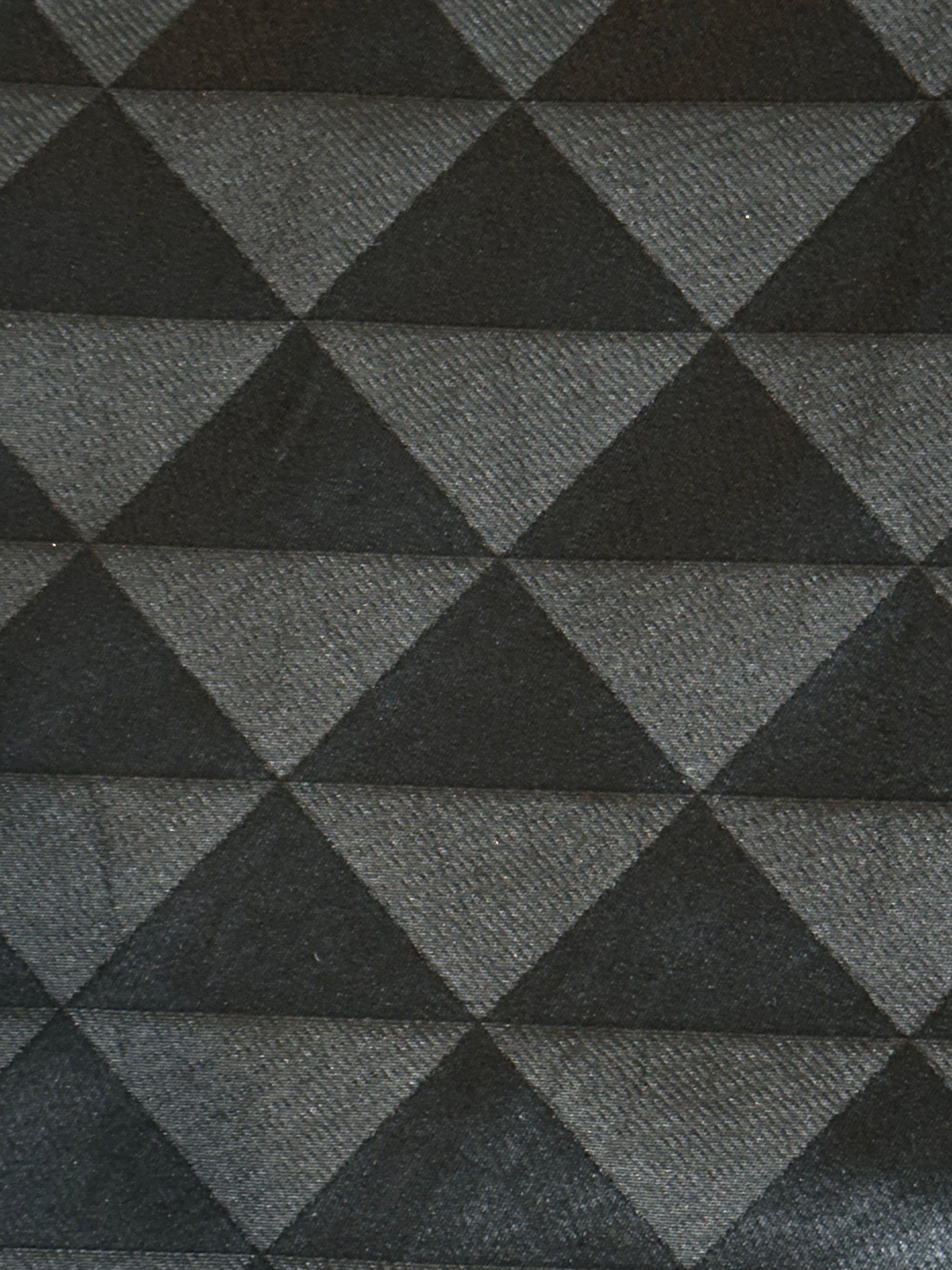A close-up of a woven fabric with a repeating geometric pattern of interlocking triangles in dark charcoal gray and medium gray.
