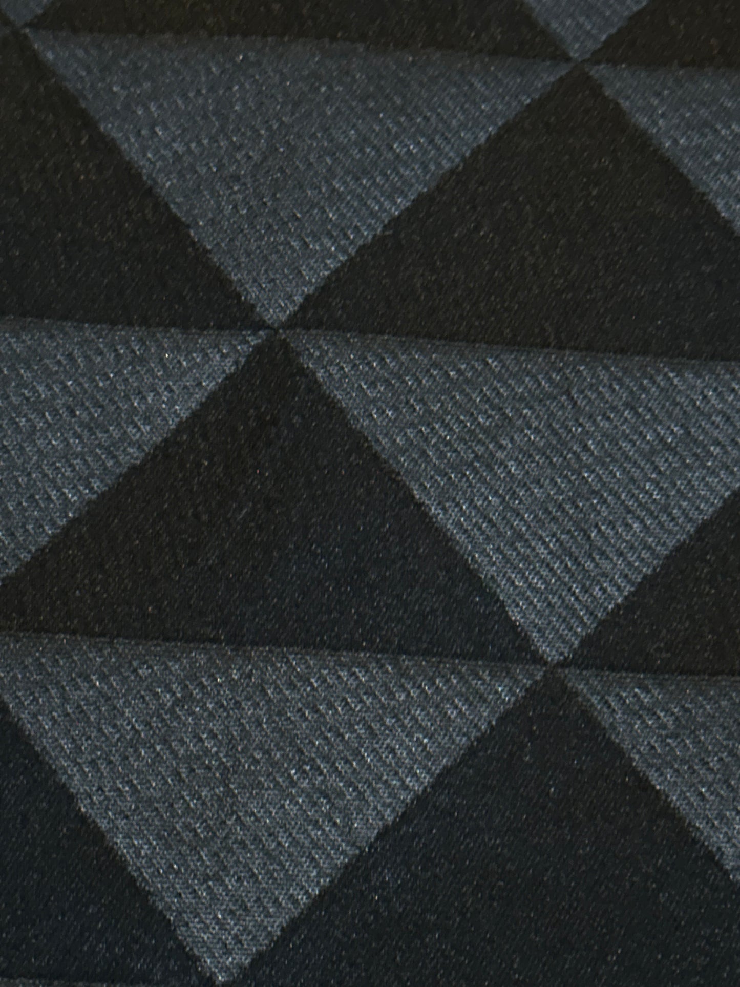 A close-up of a woven textile with a repeating geometric pattern of dark charcoal and black triangles.