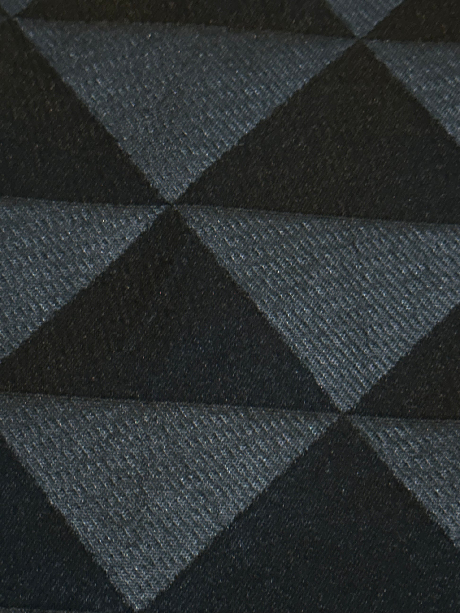 A close-up of a woven textile with a repeating geometric pattern of dark charcoal and black triangles.