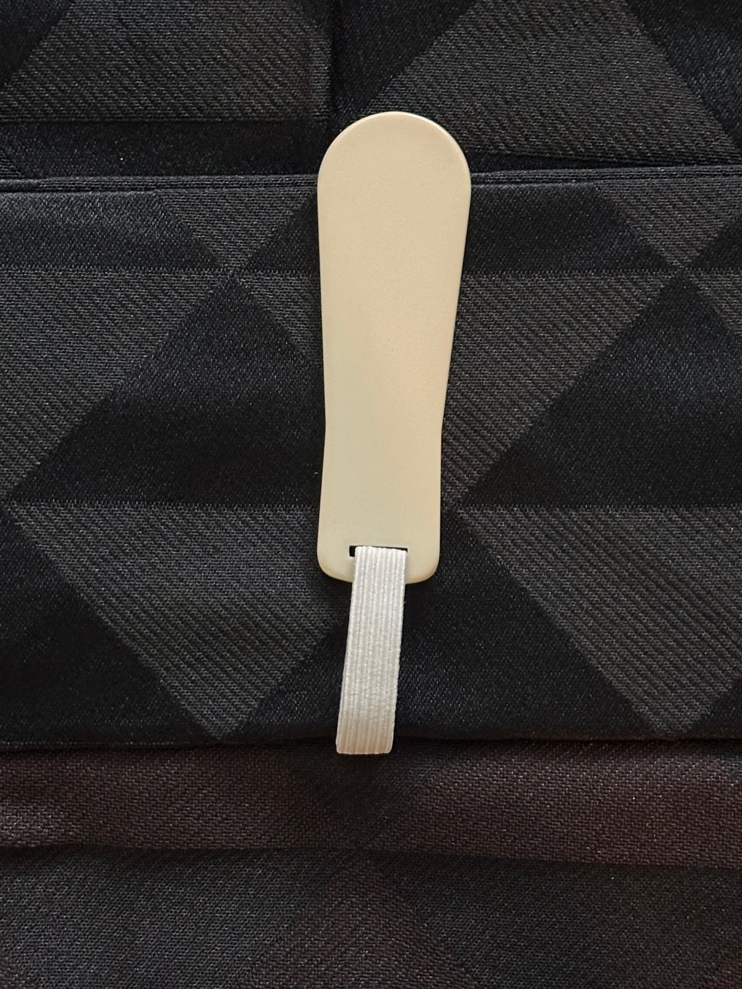 A close-up of a light beige plastic tag attached to a black and gray plaid fabric.