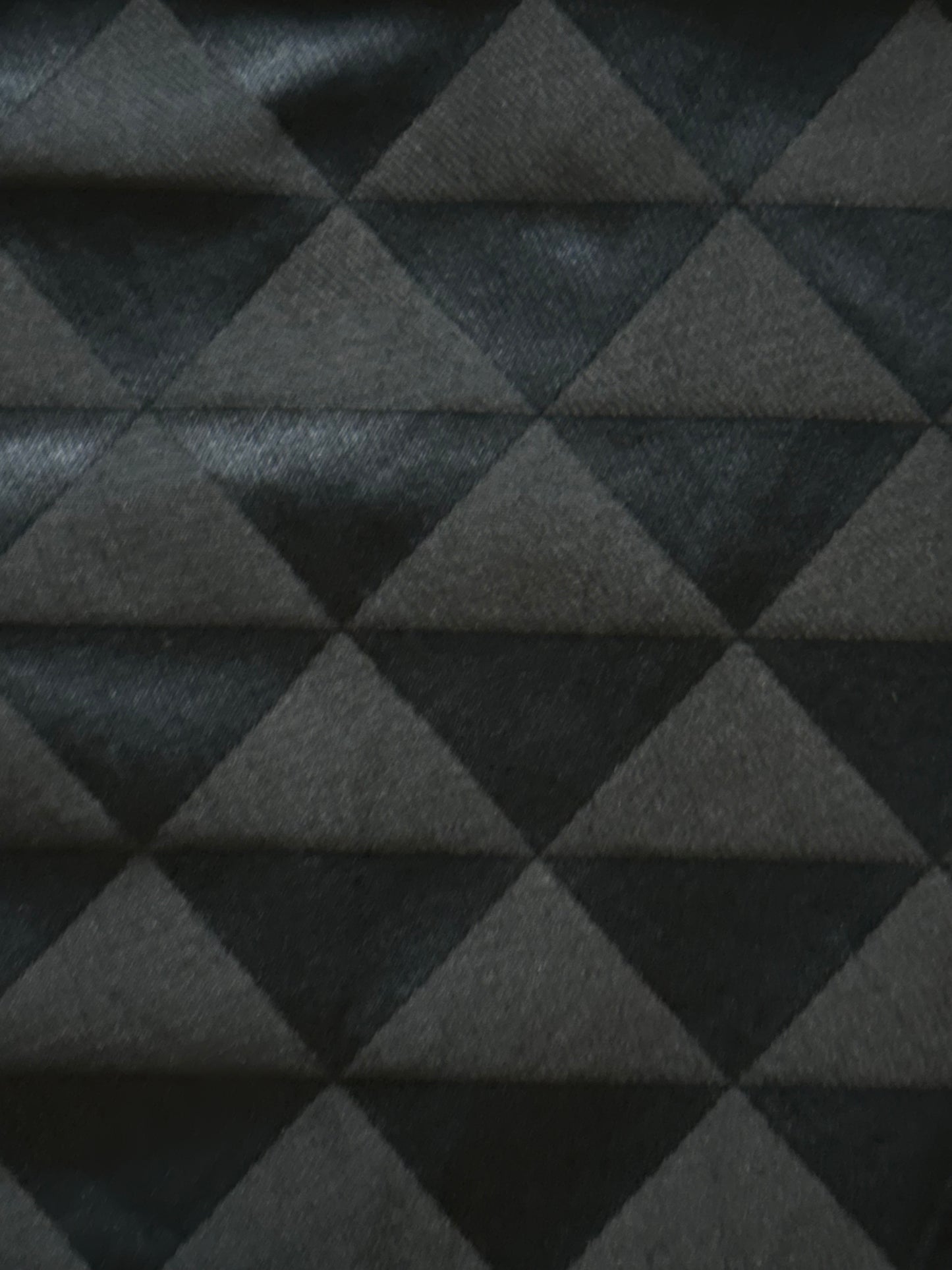 A close-up of a dark gray and black fabric with a geometric triangle pattern.