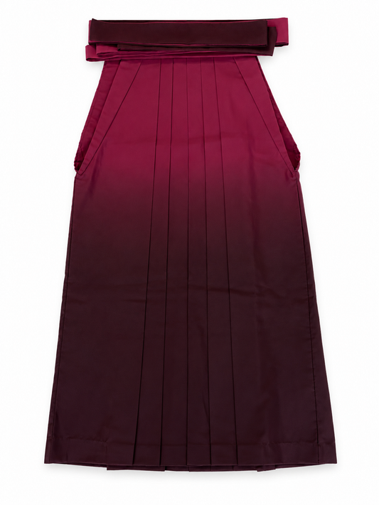 A pleated traditional Japanese hakama skirt with a wide waistband and bow detail, shown flat against a plain white background. The hakama features a deep wine red to dark burgundy ombré color gradient.