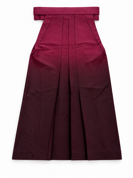 The back side of a pleated traditional Japanese hakama skirt with a wide waistband and bow detail, shown flat against a plain white background. The hakama features a deep wine red to dark burgundy ombré color gradient.