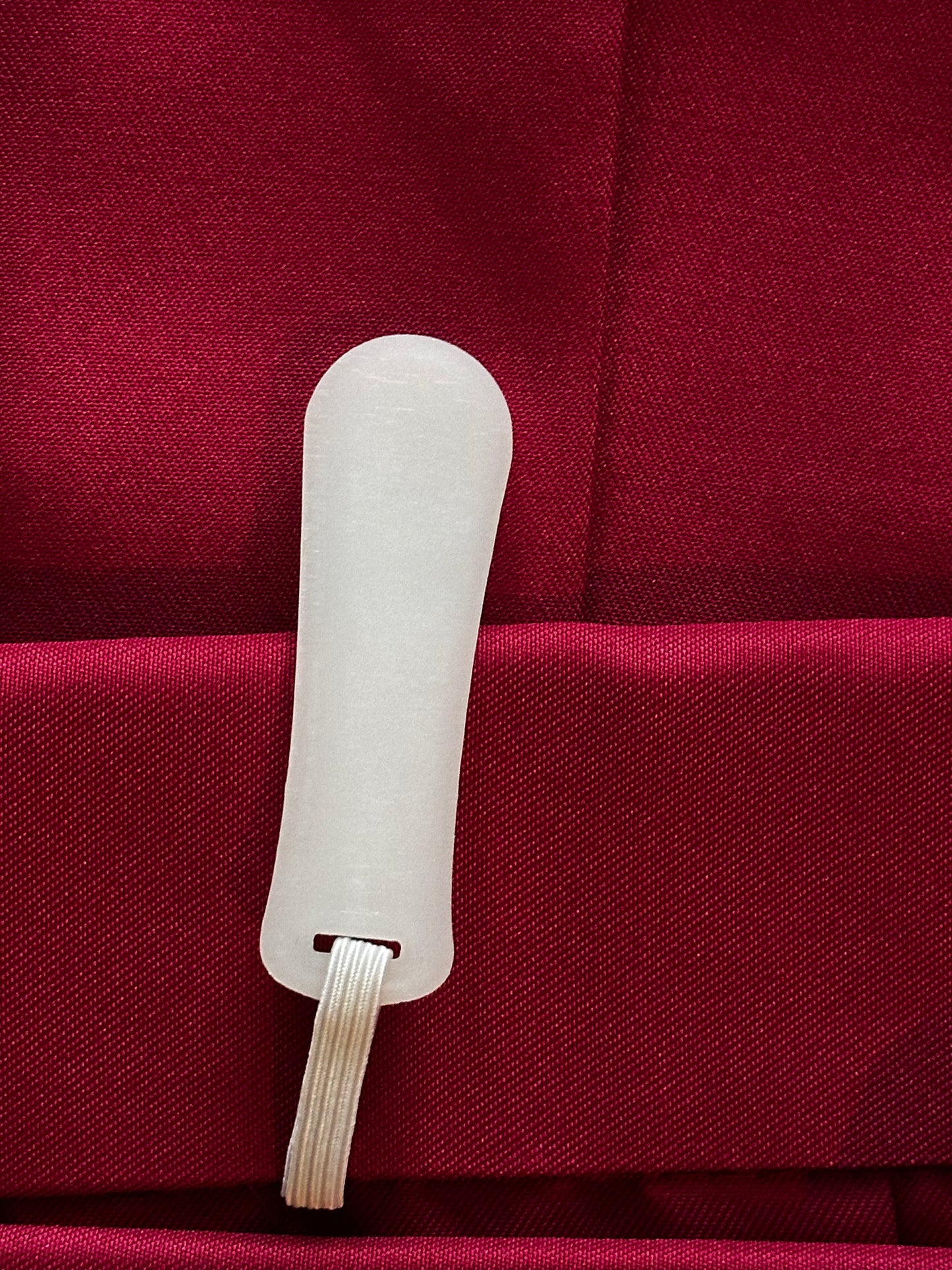 A close-up of a white plastic tool with a looped cord, resting on a textured deep red fabric background.