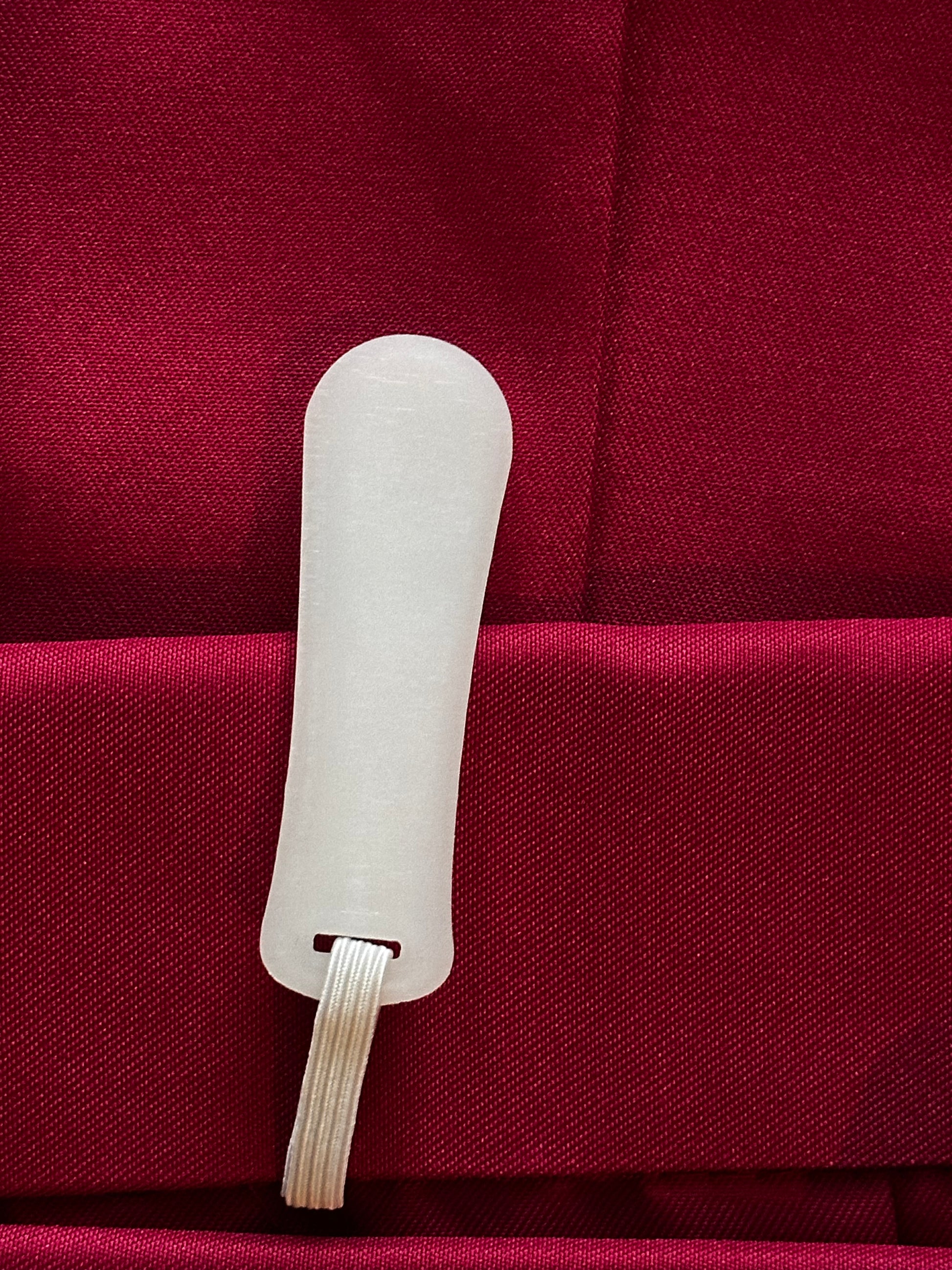 A close-up of a white plastic tool with a looped cord, resting on a textured deep red fabric background.