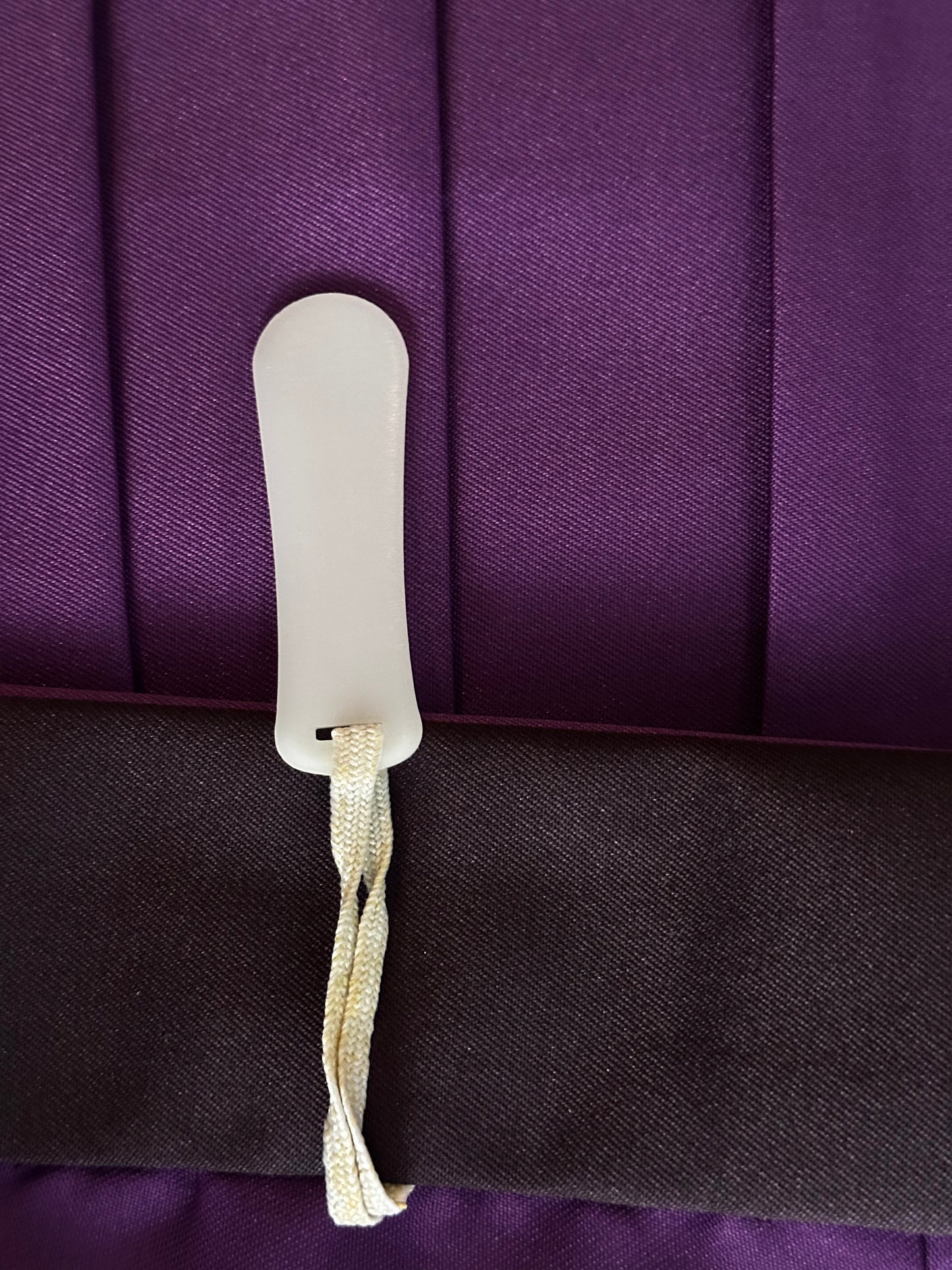 A close-up of a white plastic or acrylic clip with a cream-colored braided strap, resting on a dark purple pleated fabric background.