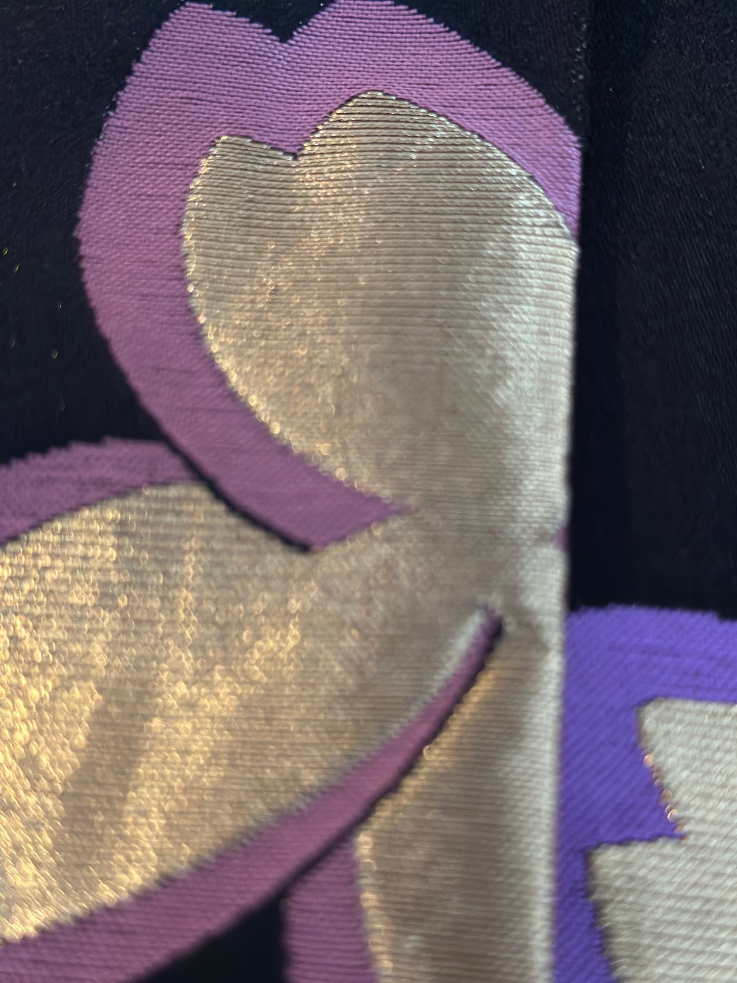 Close-up of a fabric pattern featuring metallic gold and purple embroidered floral shapes on a black background.