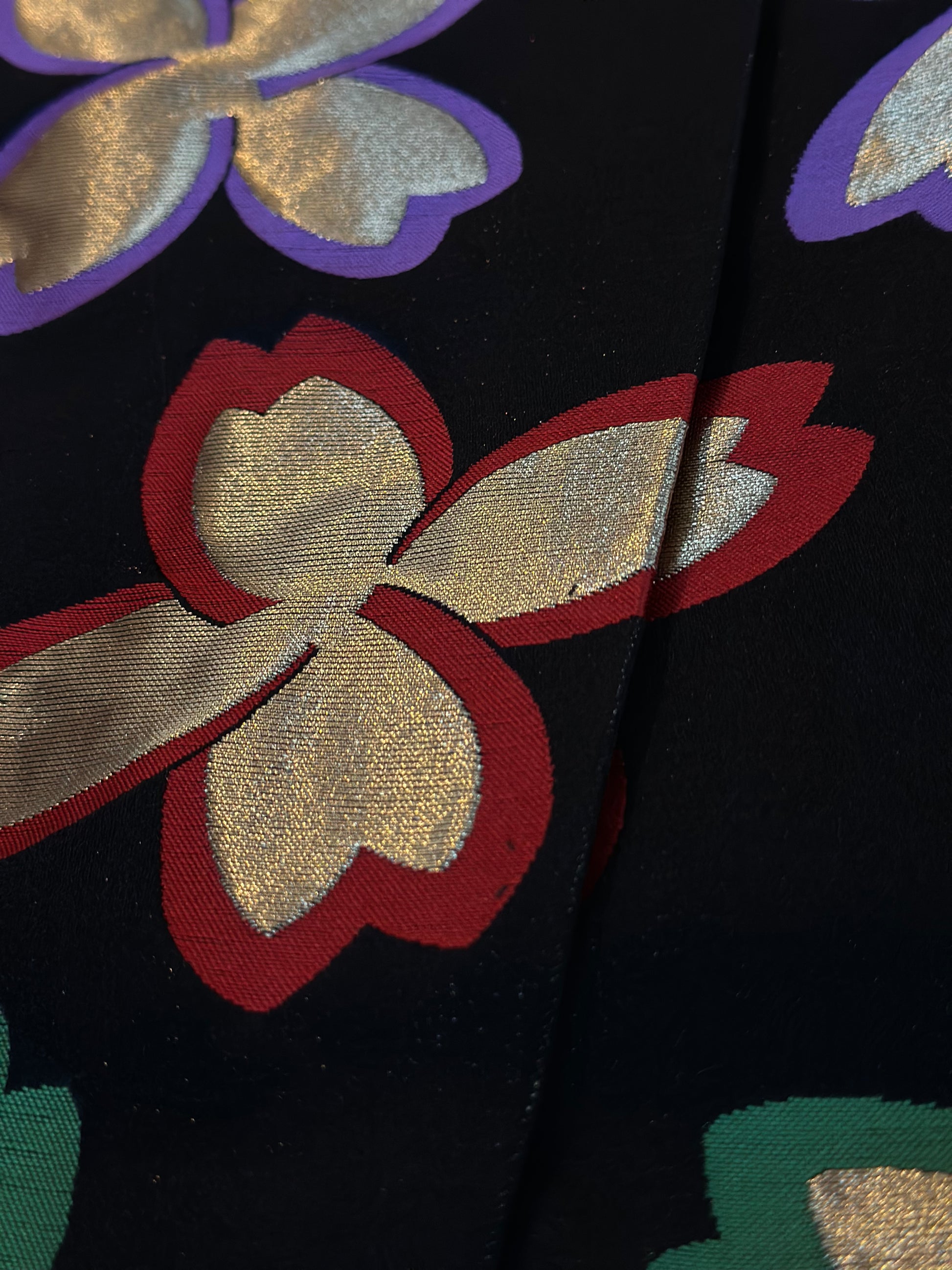 Close-up of a black fabric with a woven floral pattern featuring metallic gold petals outlined in red, purple, and green.