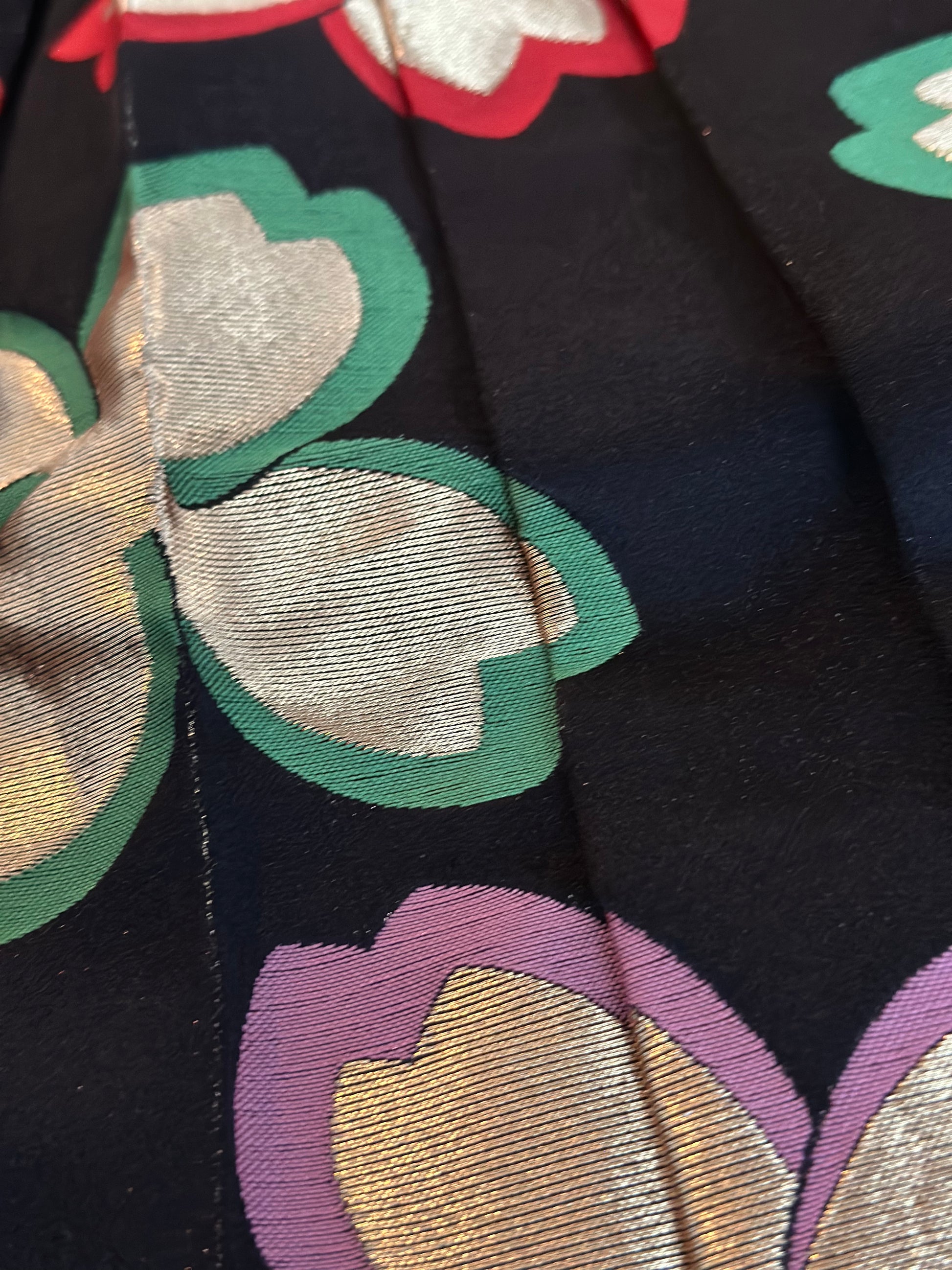 Close-up of a dark navy or black fabric with a woven floral pattern in metallic gold, green, purple, and red.