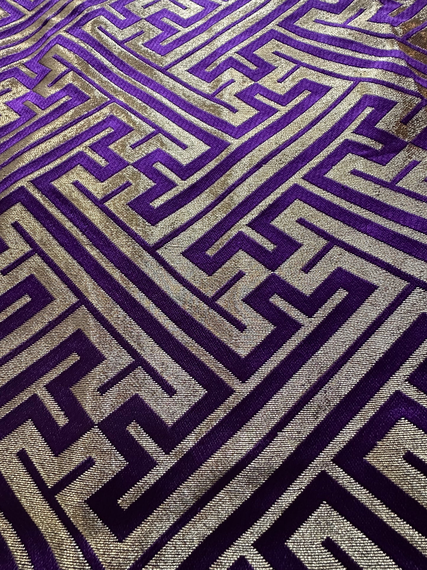 A close-up of a hakama fabric with a geometric Greek key pattern in deep purple and metallic gold.