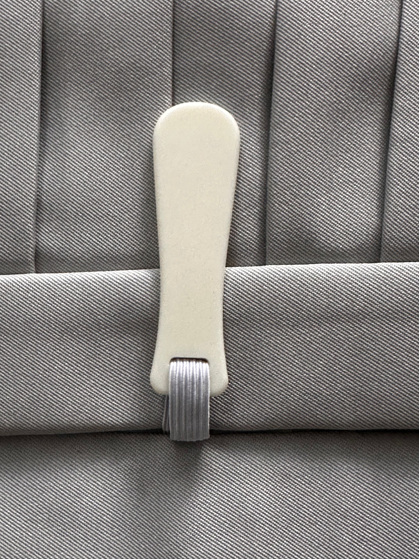 A close-up of a light beige plastic fastener attached to a gray pleated fabric background.