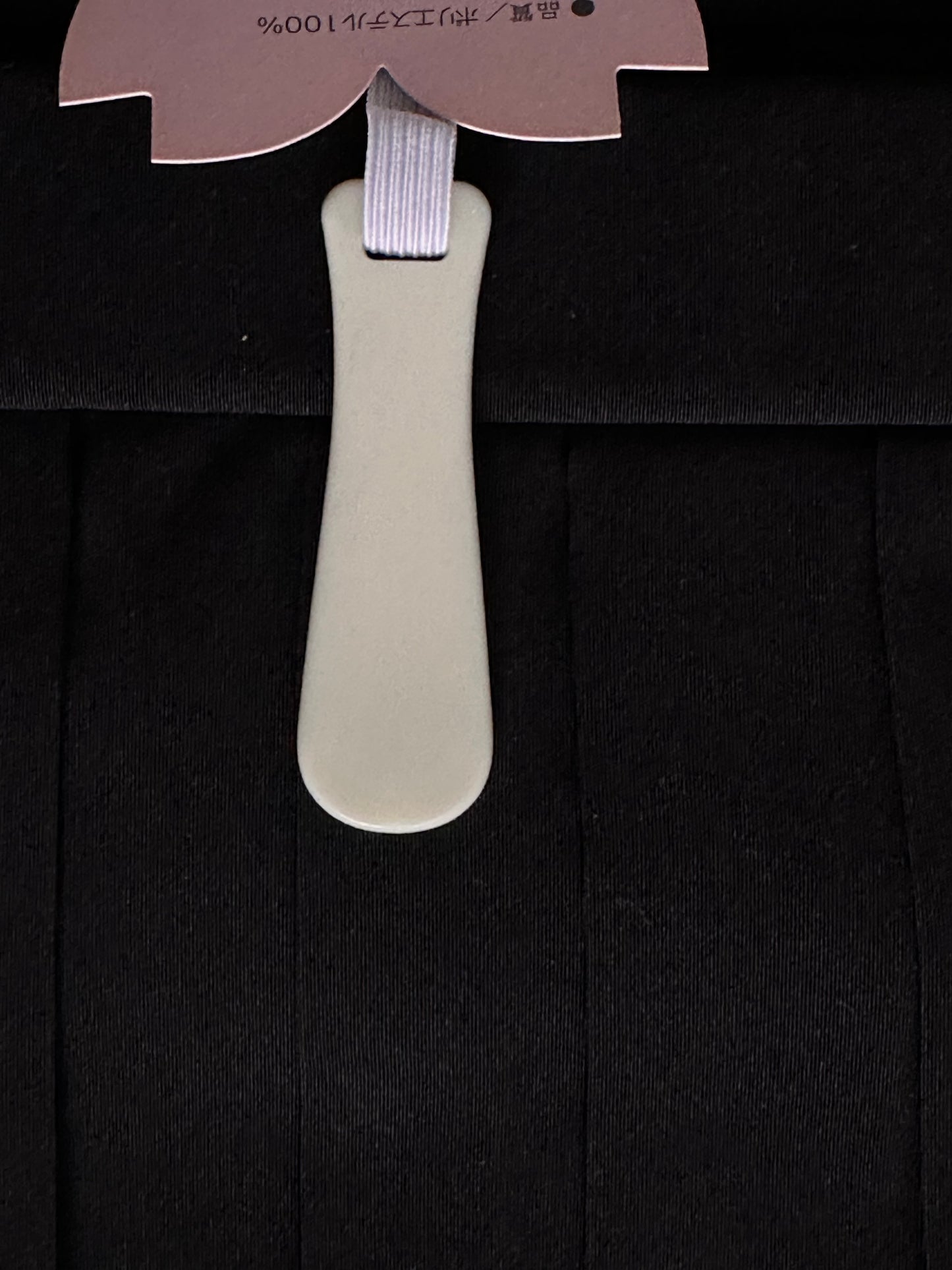 A close-up of a black hakama fabric, featuring a light beige plastic hanger insert with a lavender elastic strap and a pink paper tag at the top.