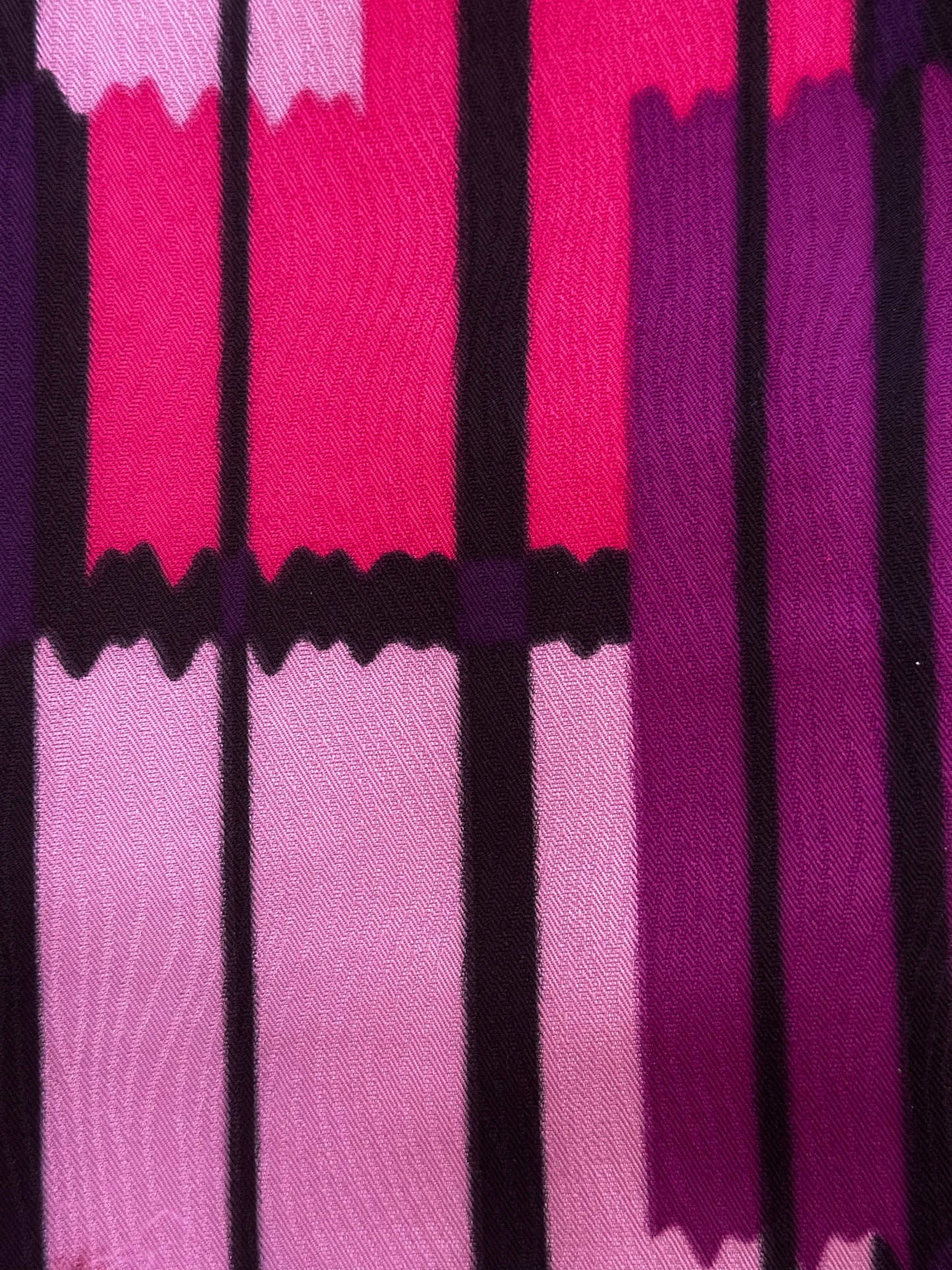 A close-up of a woven textile with an abstract geometric pattern in pink, magenta, purple, and black vertical blocks.