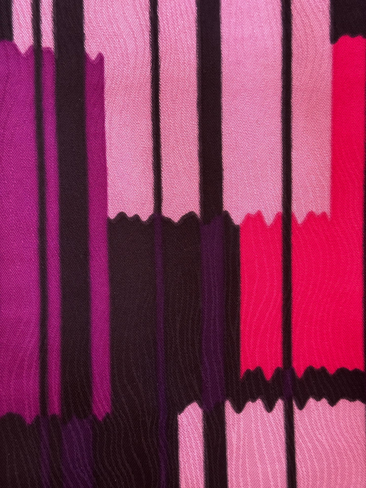 A close-up of a patterned fabric featuring vertical stripes in shades of pink, magenta, purple, and black.