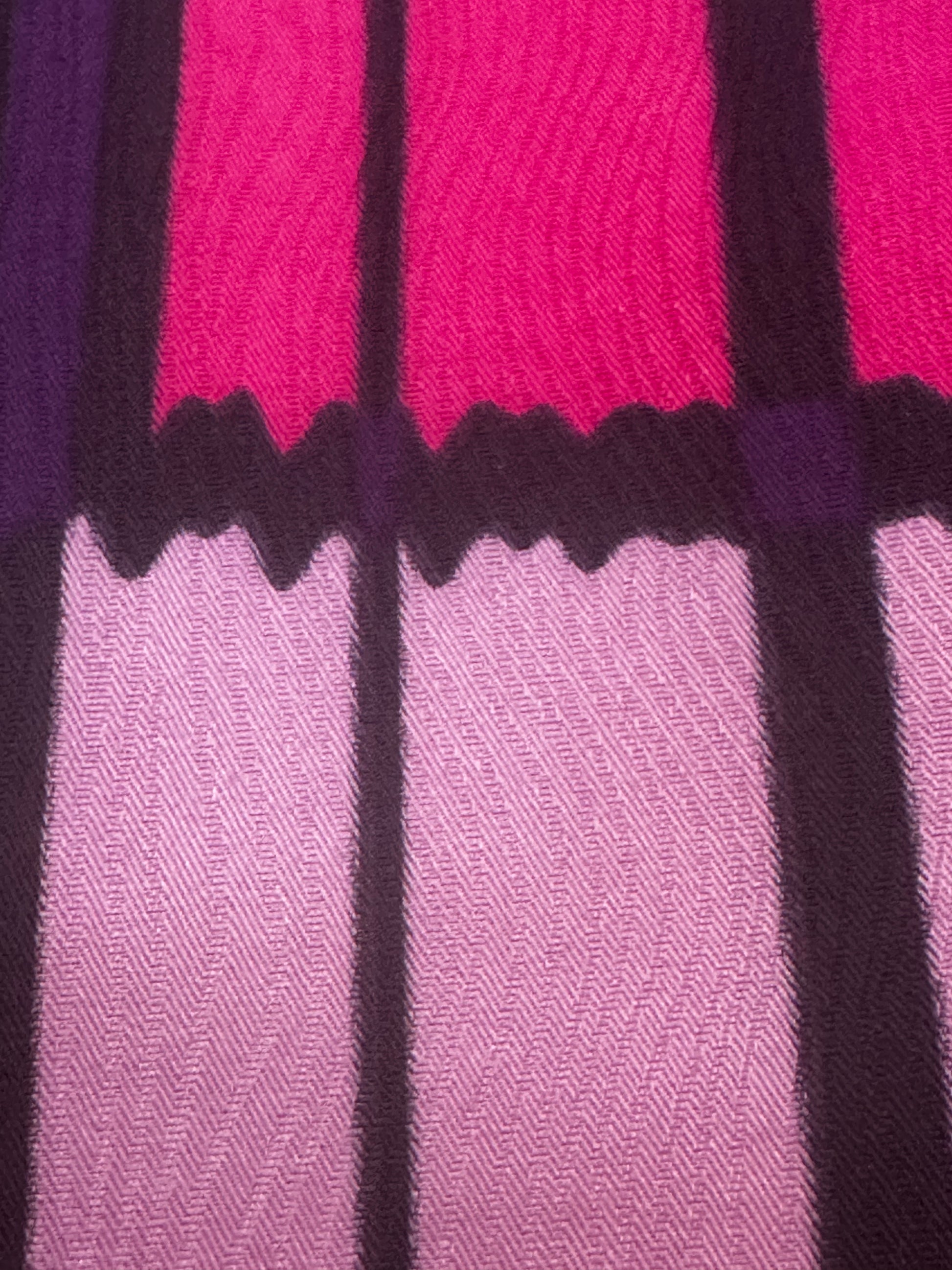 A close-up of a woven textile pattern featuring alternating vertical panels in bright pink, light lavender, and deep purple, separated by thick dark purple vertical stripes and a scalloped wavy border.
