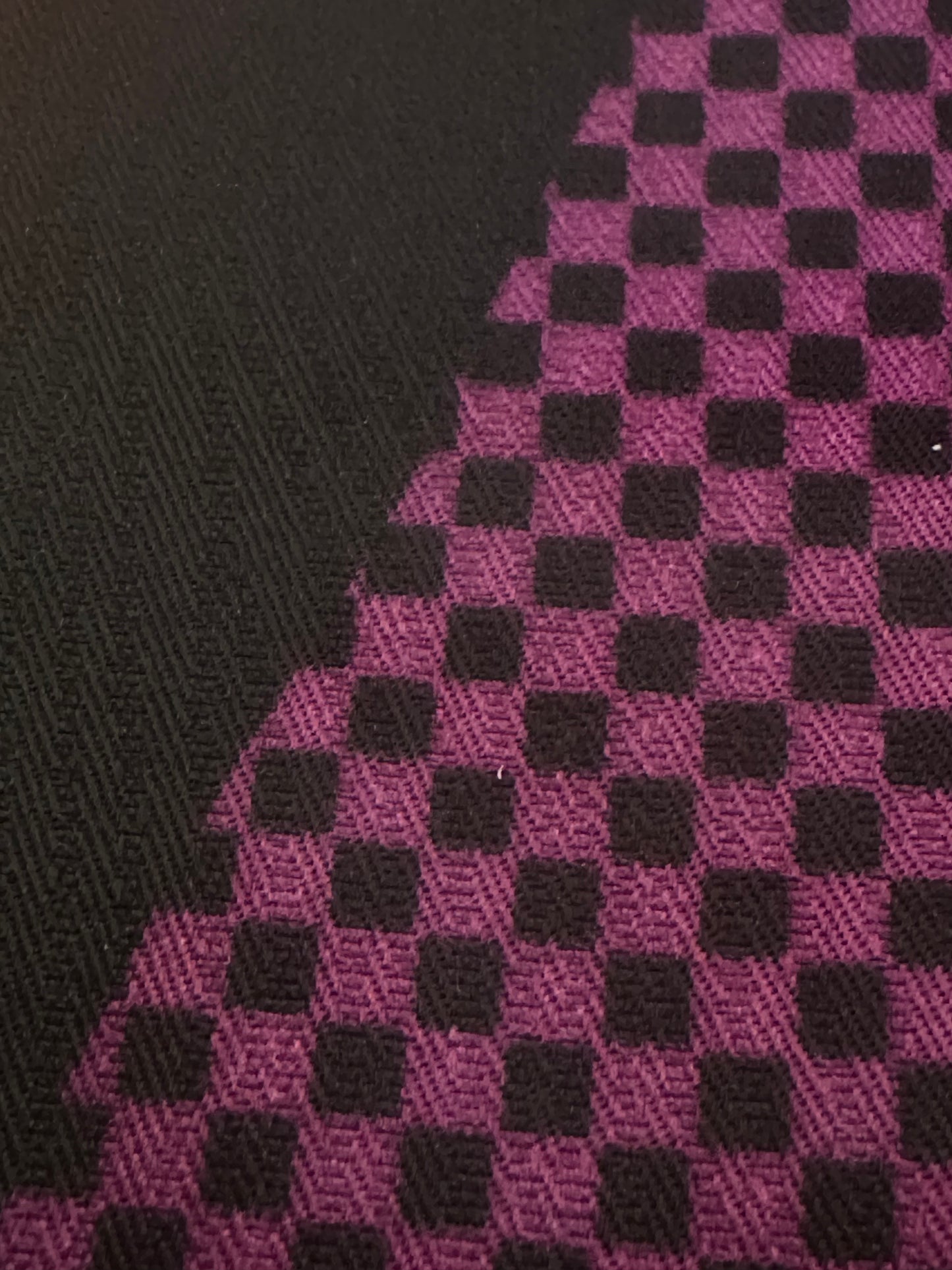 A close-up of woven fabric showing a black and magenta checkerboard pattern, with a solid black textured section on the left.