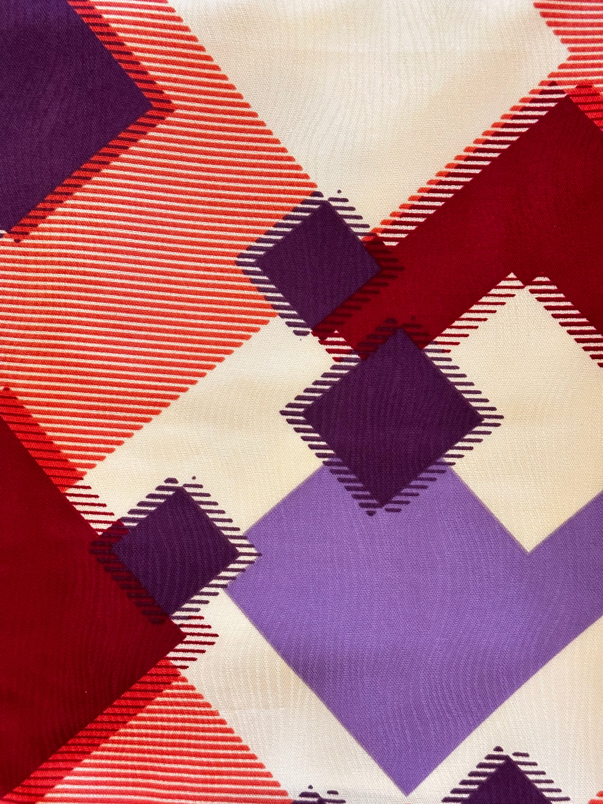 A close-up of a woven fabric with a geometric plaid pattern in red, purple, and cream.