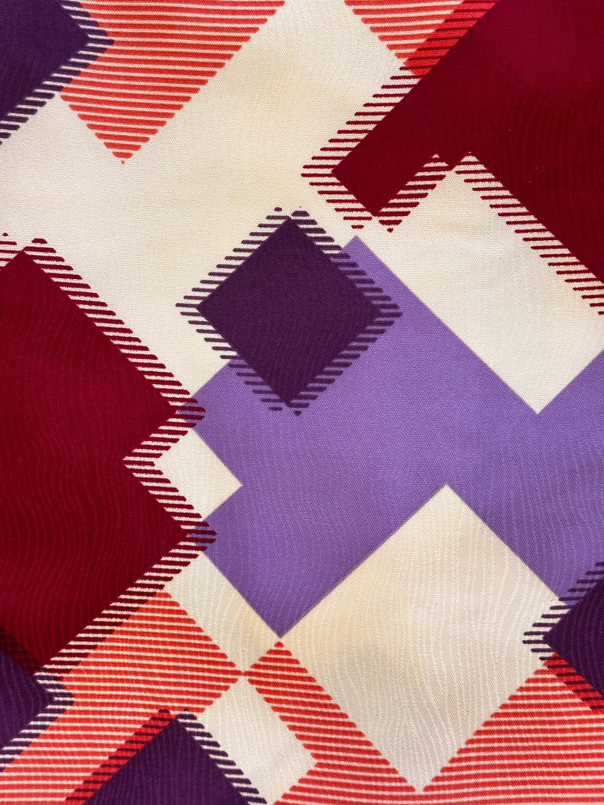 A close-up of a woven fabric with a geometric plaid pattern in burgundy red, lavender purple, and cream.